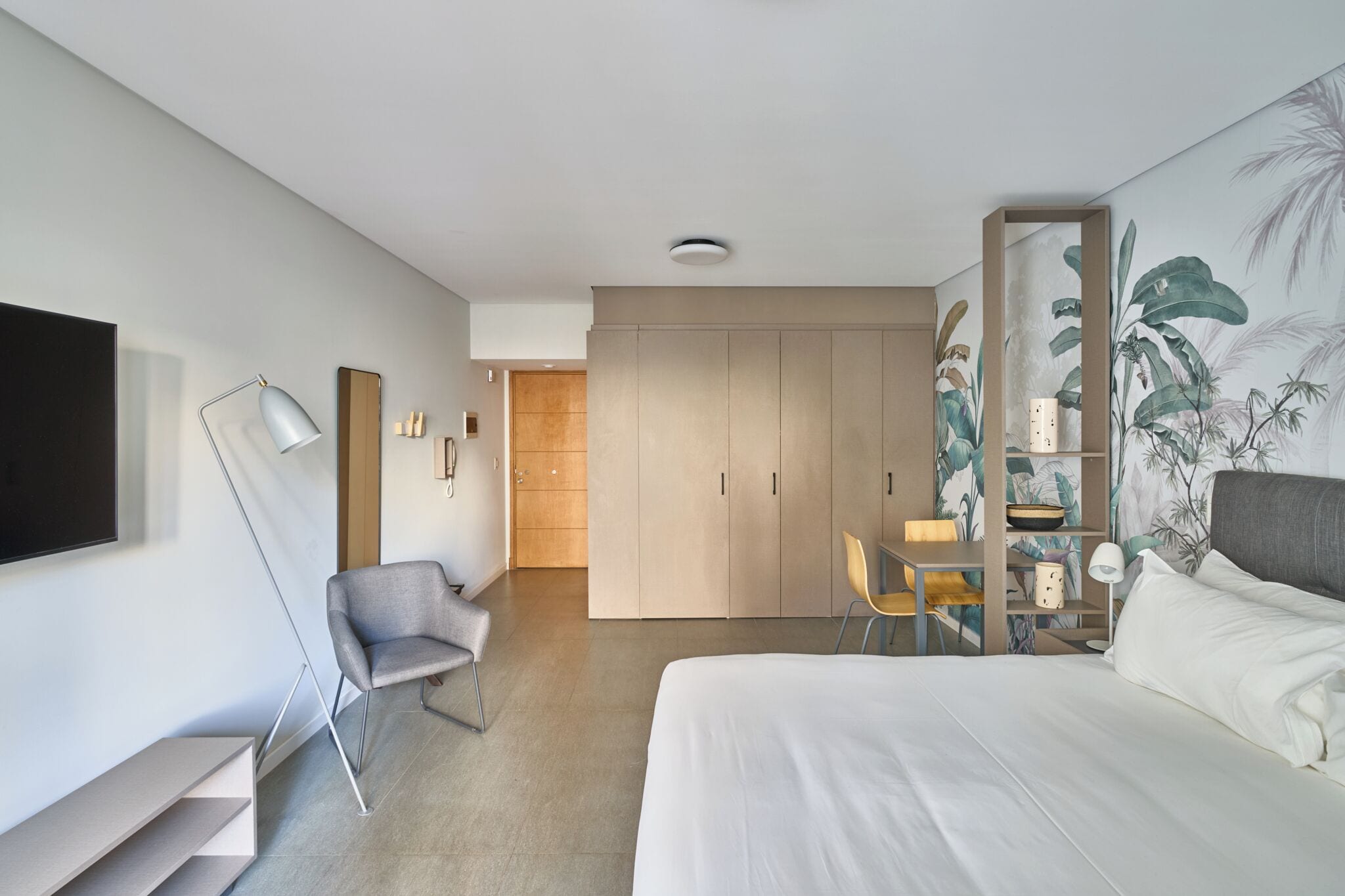 Una habitación de hotel moderna con cama, escritorio, silla, armario y televisor.