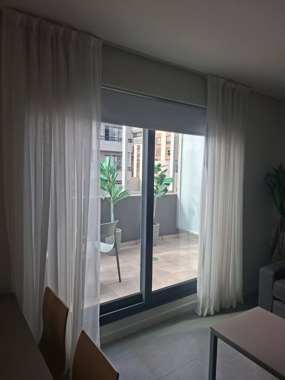 Een kamer met een grote schuifdeur die leidt naar een balkon, een stoel, een tafel en een bloempot.