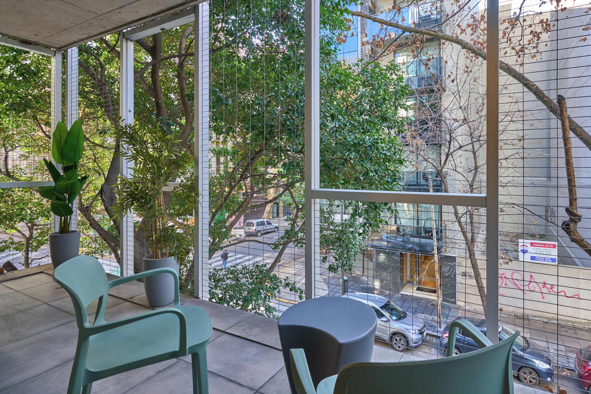 A modern indoor space with large windows, potted plants, and seating arrangements.