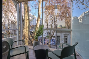 A balcony with chairs, a potted plant, and a view of trees and buildings. - Alma Rentals Sol Palermo (Buenos Aires)