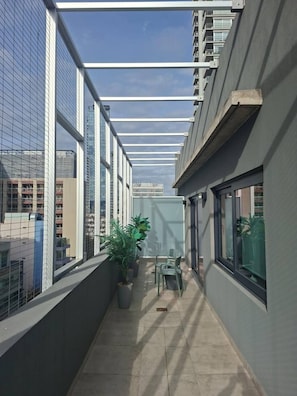 Un couloir étroit doté d’un plafond en verre, de plantes en pot et d’une petite table entourée de chaises.
