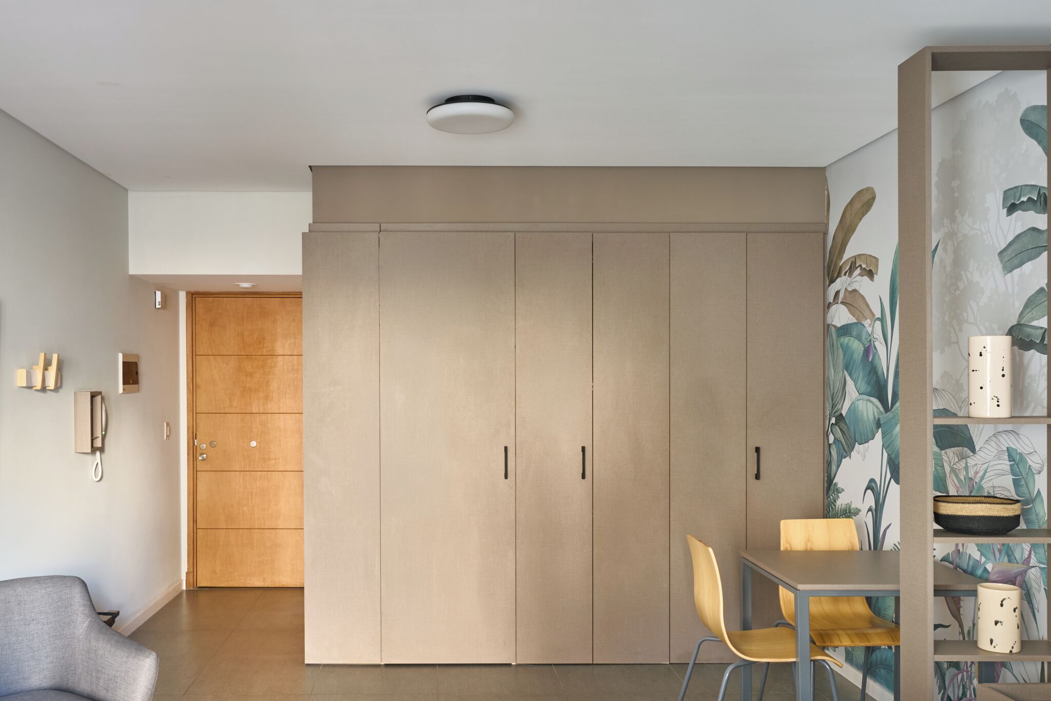 A modern interior with a wardrobe, a dining area, and a shelf with decorative items.
