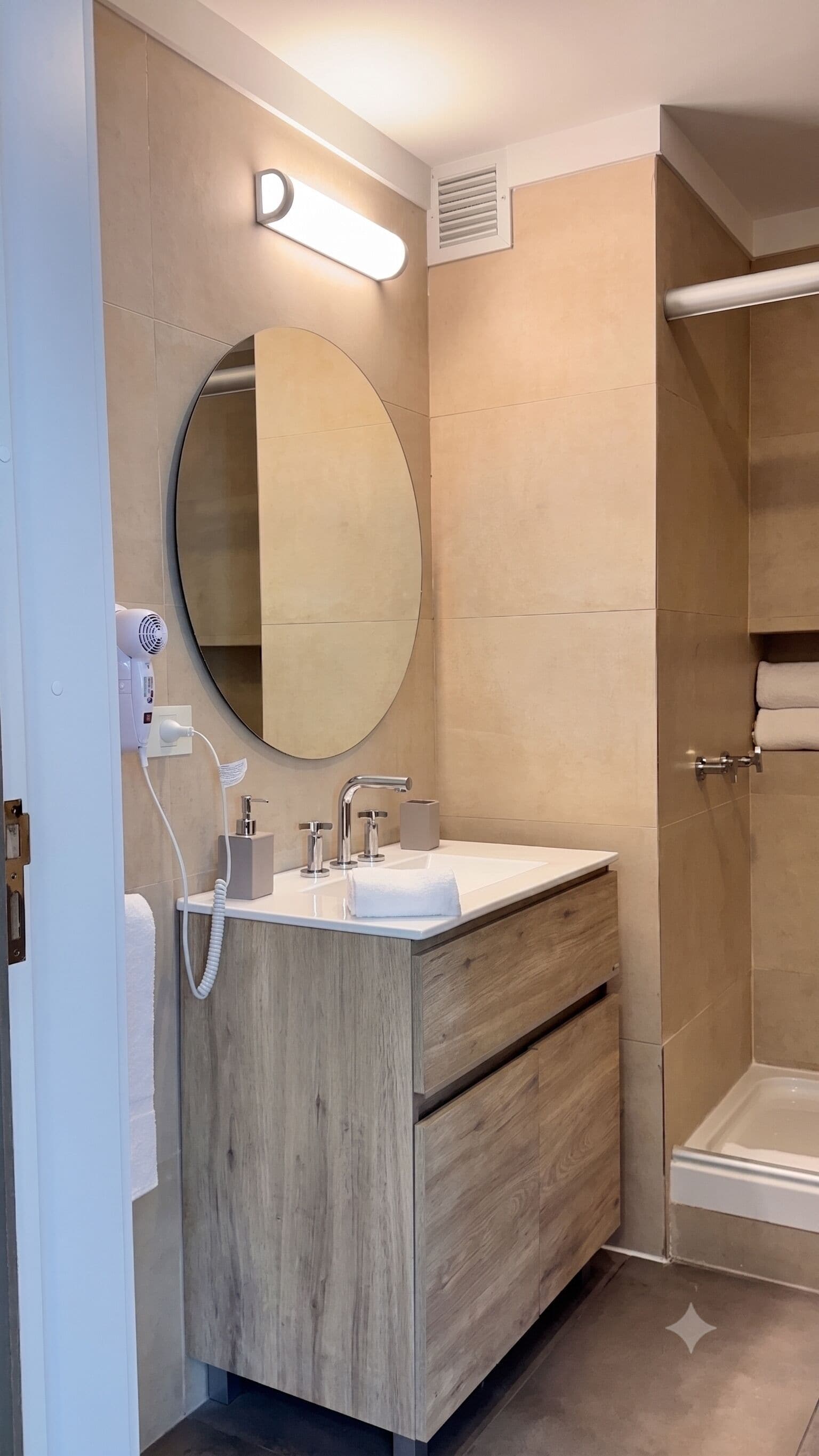 A modern bathroom with a round mirror, a sink with a towel, and a shower area.
