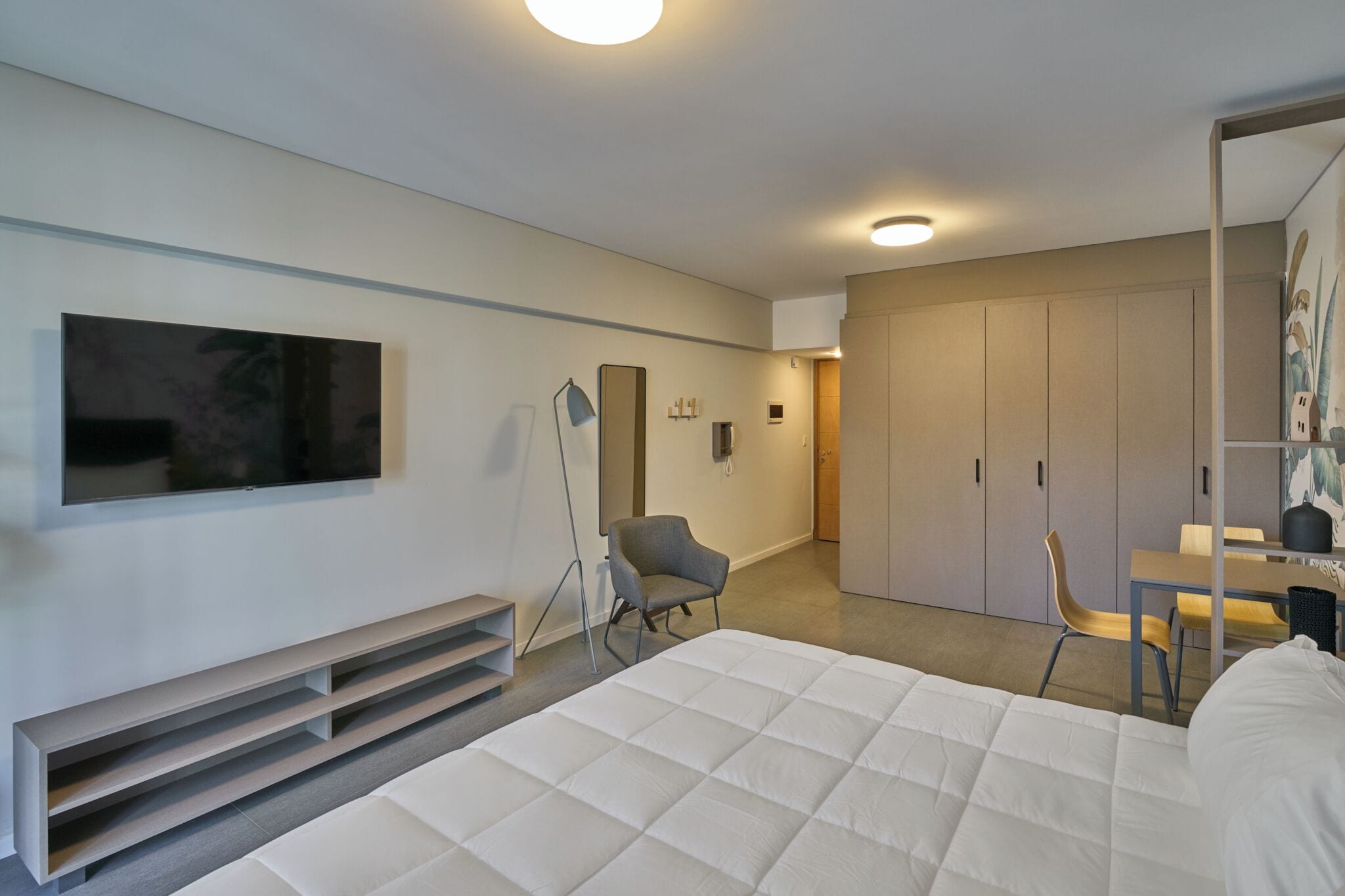 Una habitación de hotel moderna con una cama, un escritorio, una silla, un televisor y un armario.