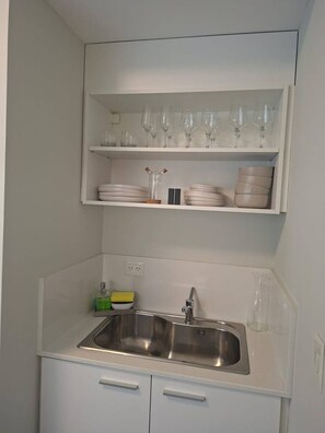 Una cocina con un lavamanos doble, armarios blancos y repisas superiores con vasos y platos.
