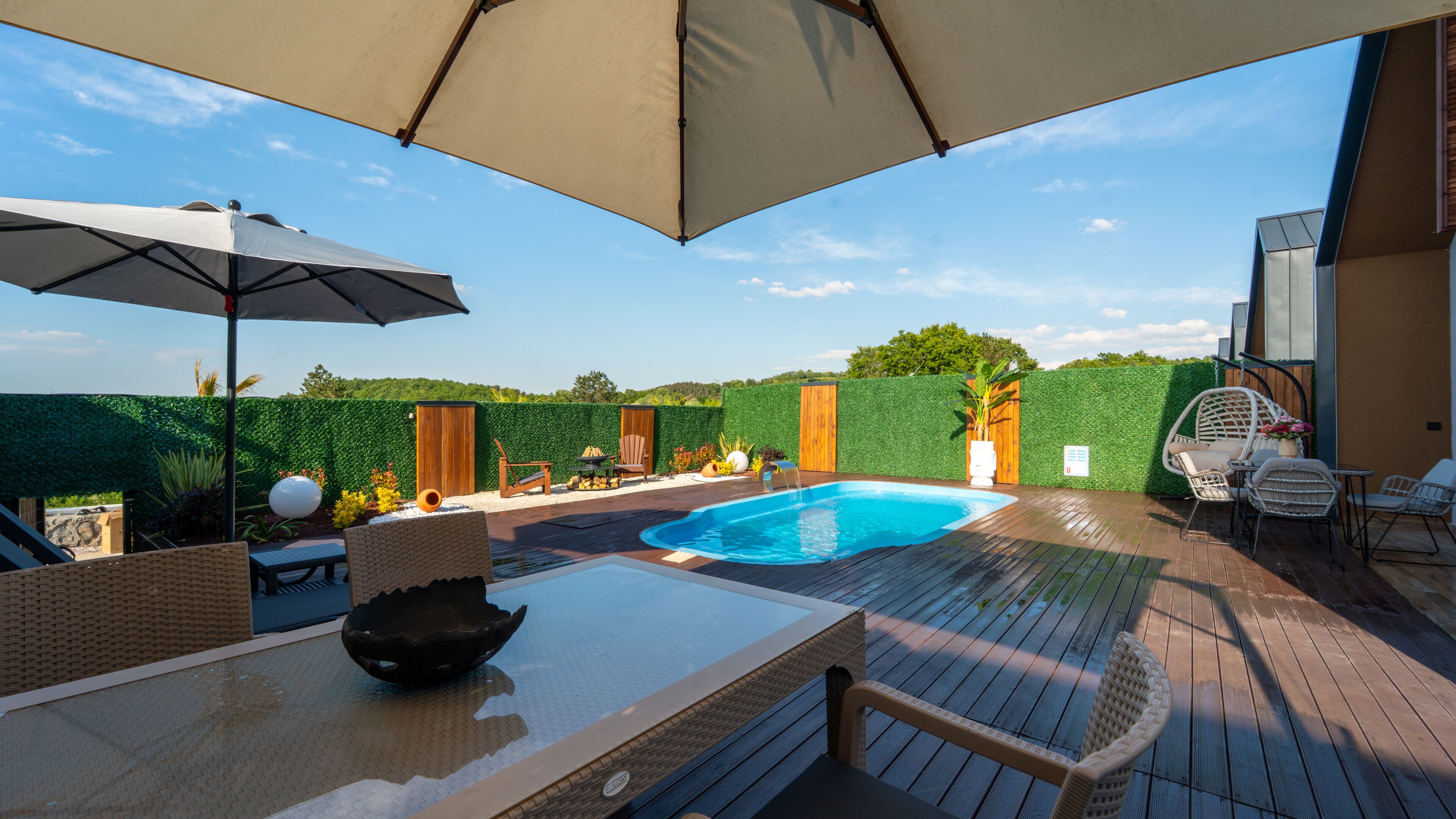 Area piscina con pavimento in legno, mobili da esterno e un muro di siepe verde.