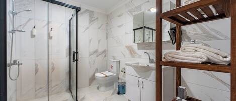 Un baño moderno con cabina de ducha de vidrio, inodoro, lavamanos y estante de madera con toallas.