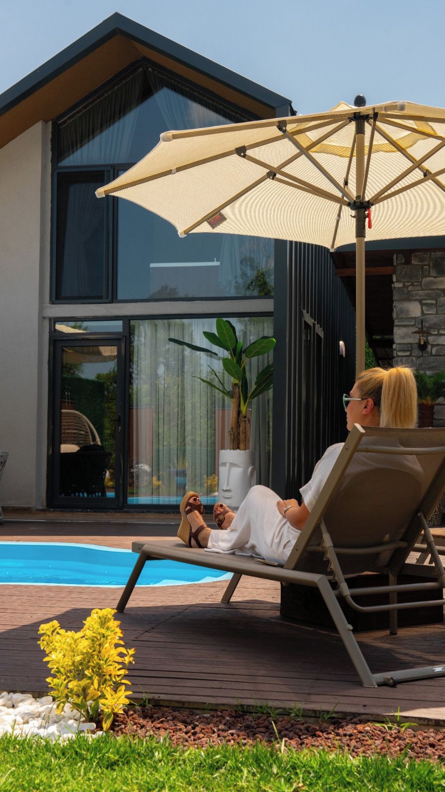 Et moderne hus med swimmingpool, liggestol og stor parasol.