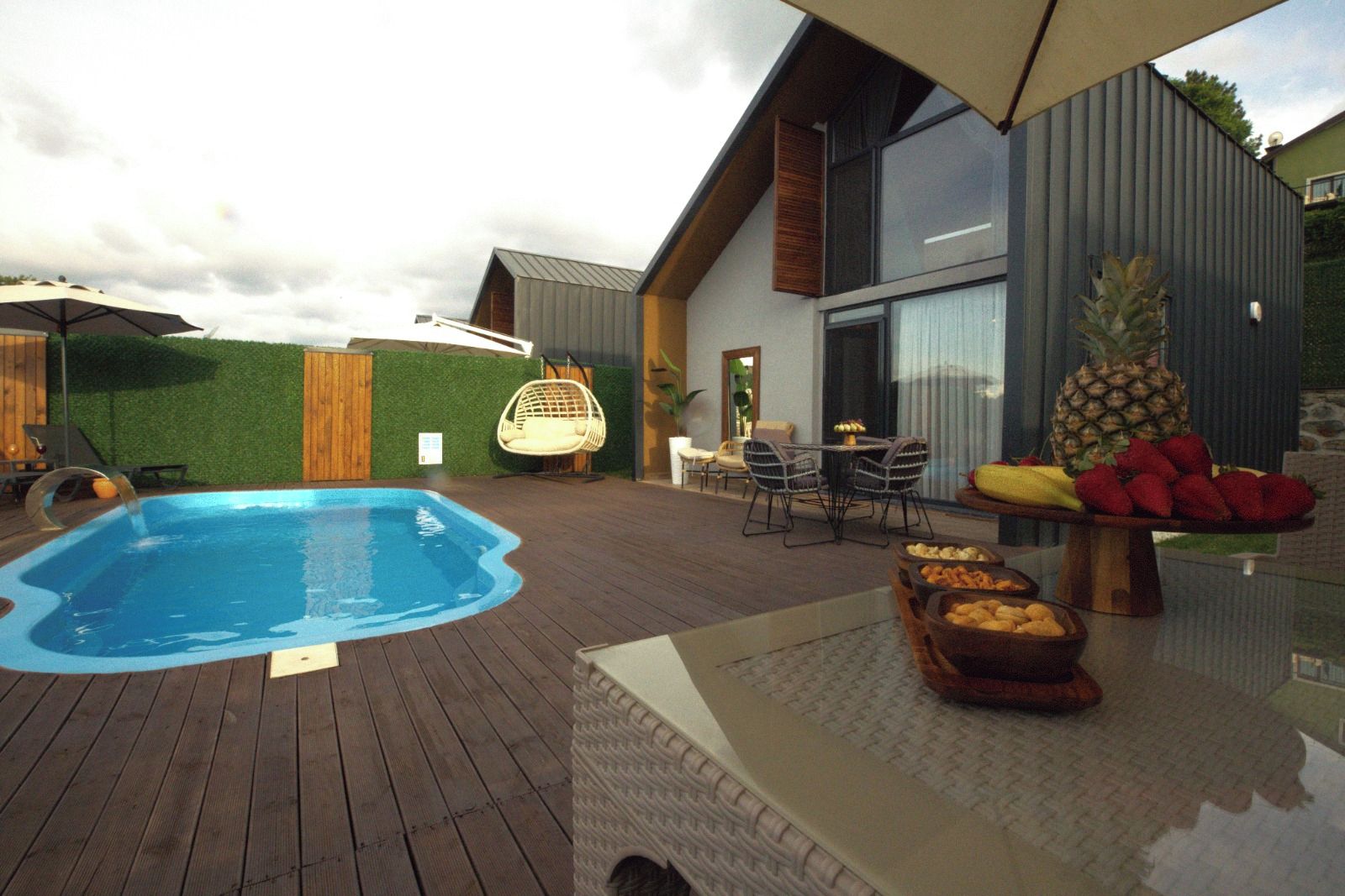 A swimming pool with a wooden deck, outdoor furniture, and a fruit display.