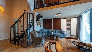 Amplia sala de estar con una escalera, un conjunto de sofás, una mesa de centro y una mesa de comedor.