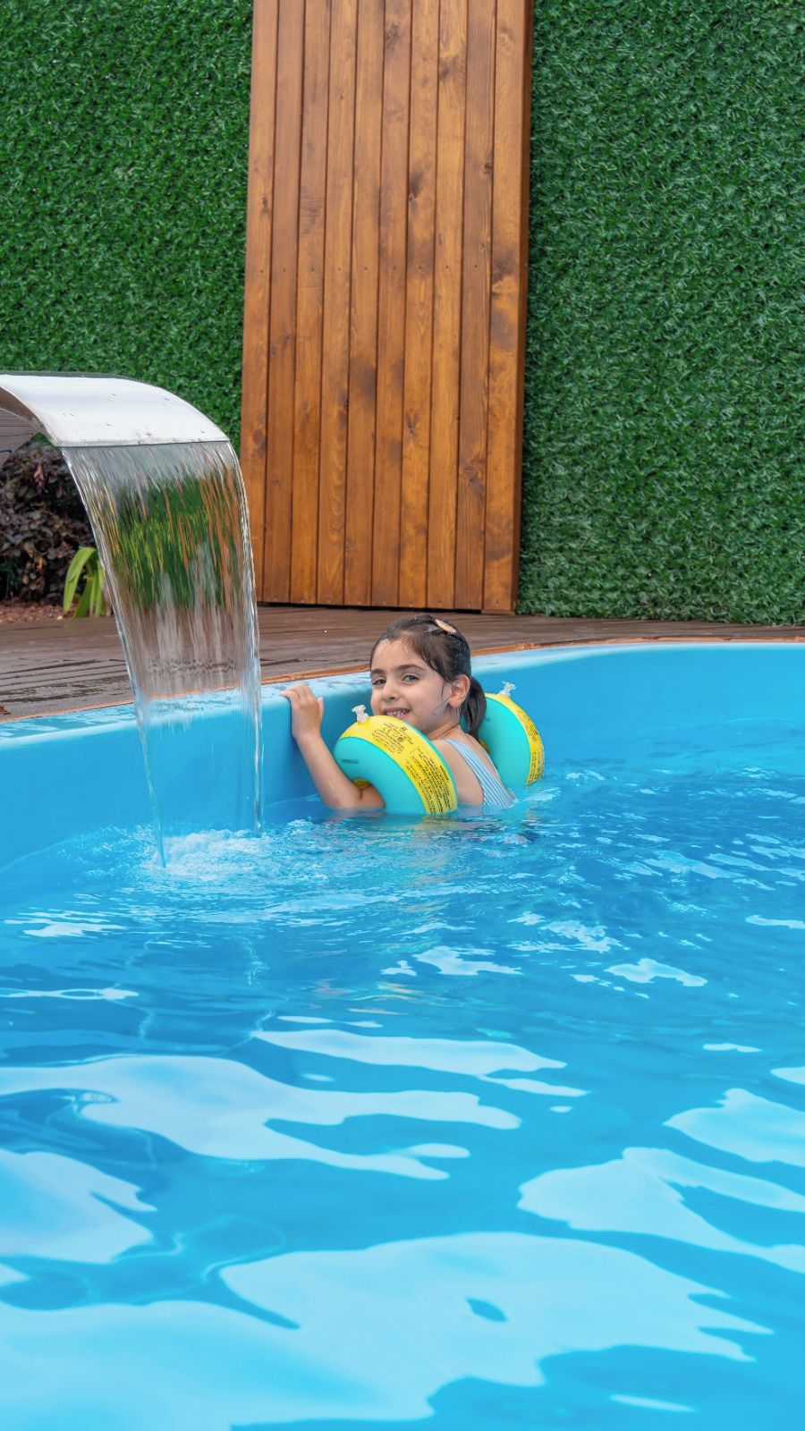 A child in a swimming pool with a water feature.