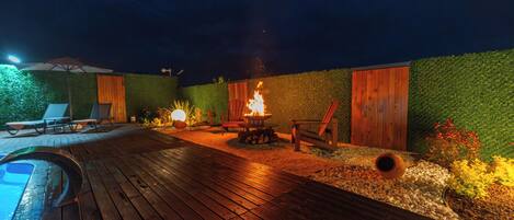 Eine Holzterrasse mit Pool, Liegestühlen, Feuerstelle und einer grünen Wand.