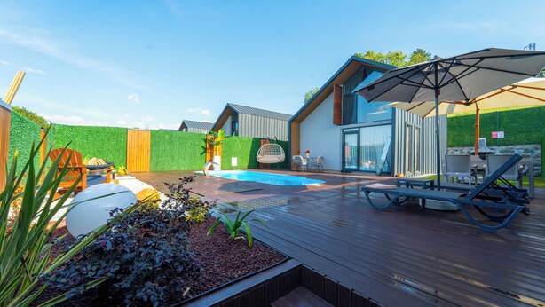 Un área de piscina moderna al aire libre con un deck de madera, sillones de descanso y una zona de estar cubierta.