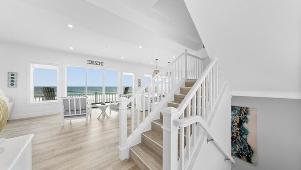 Geräumiger Innenraum mit einer Treppe zu einem Balkon mit Meerblick, einem Essbereich und Blick auf den Strand.