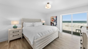 Ein Schlafzimmer mit Bett, Nachttischen, einem Gemälde und Blick auf den Strand.