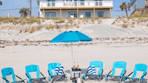 Ein Strandgrundstück mit einem zweistöckigen Gebäude, einem Sandstrand und Liegestühlen sowie einem blauen Sonnenschirm.