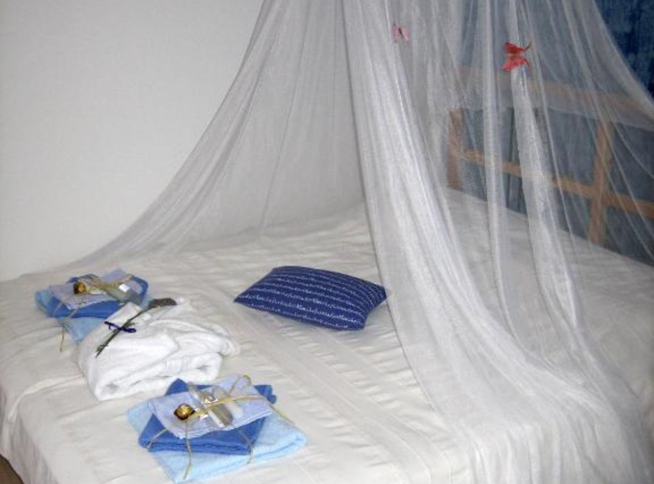 Una cama con sábana blanca, almohada azul y manta blanca doblada encima.