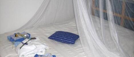 Una cama con sábana blanca, almohada azul y manta blanca doblada encima.
