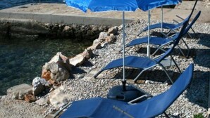 A beach with a blue umbrella, lounge chairs, and a rocky shoreline. - Apartments Mediterraneo Blues (Sibenik)