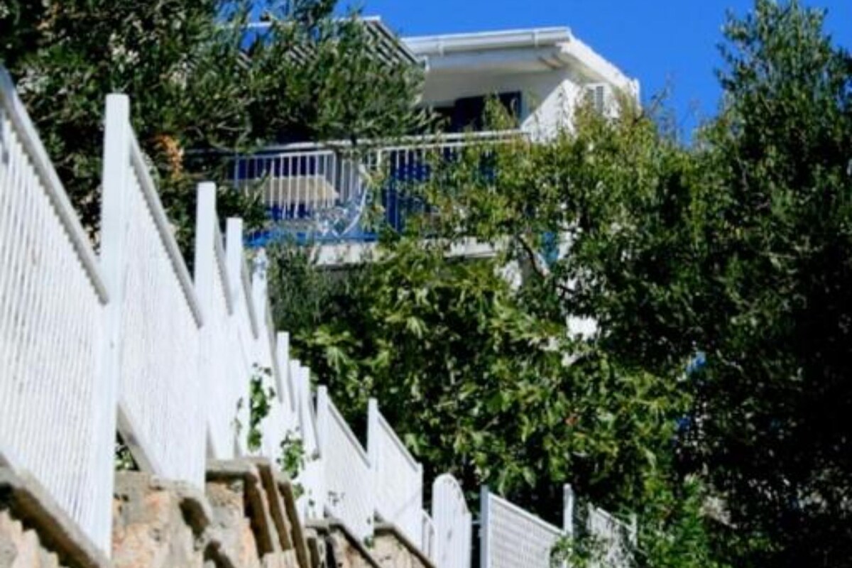 Ein weißes Gebäude mit Balkon, umgeben von viel Grün und einem weißen Zaun.