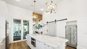 Een moderne keuken met een groot eiland, houten vloeren, witte kastjes en hanglampen.