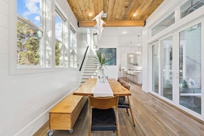 A dining area with a wooden table, chairs, a vase, and a staircase leading to another level. - Home w/ Carriage, Private Pool and Peloton (Santa Rosa Beach)