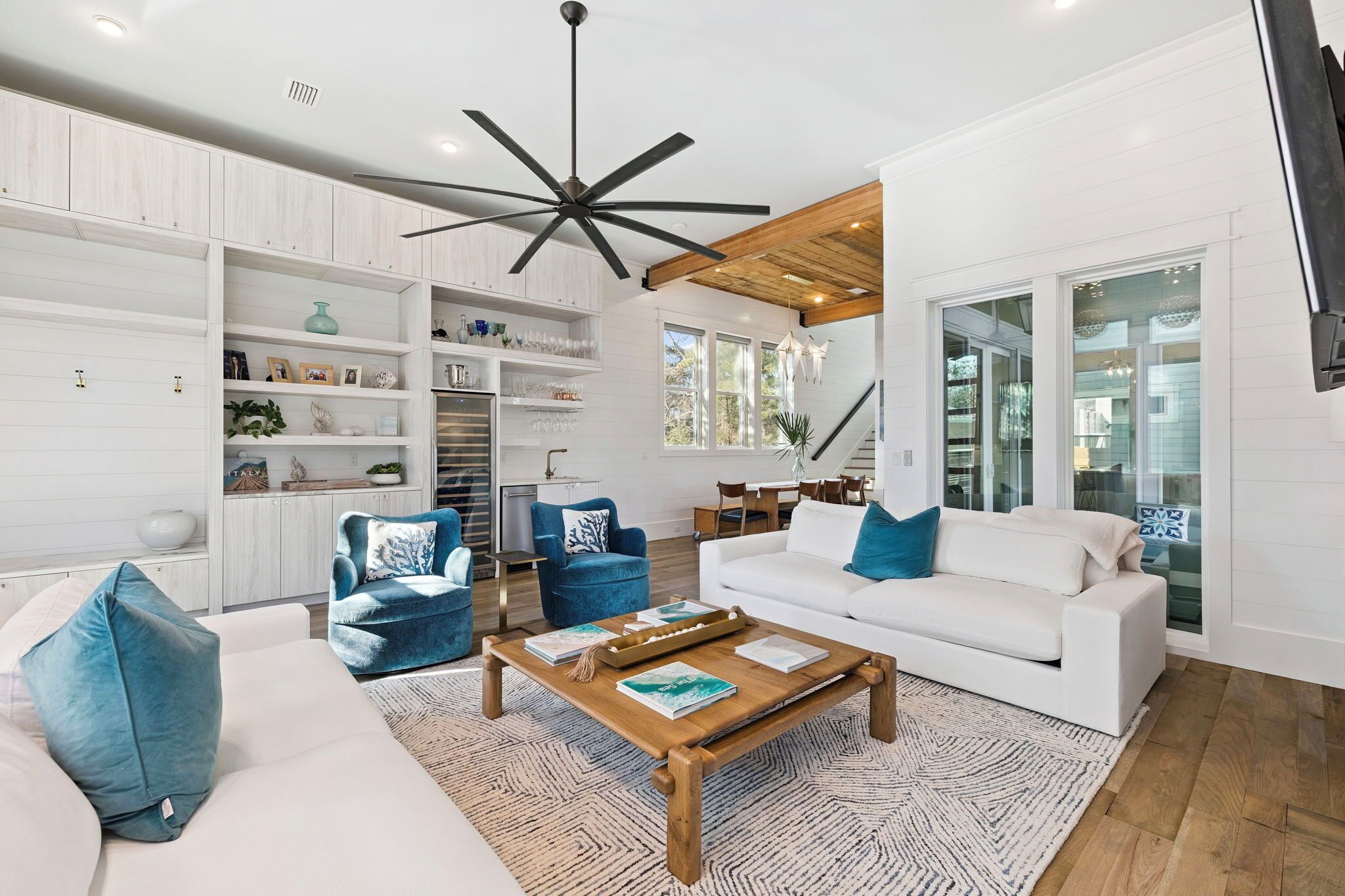 A modern living room with a white sofa, blue armchairs, a wooden coffee table, and a ceiling fan.
