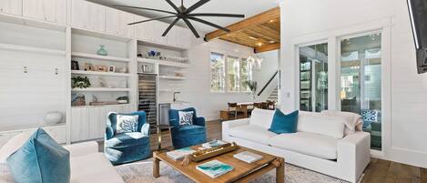 A modern living room with a white sofa, blue armchairs, a wooden coffee table, and a ceiling fan.
