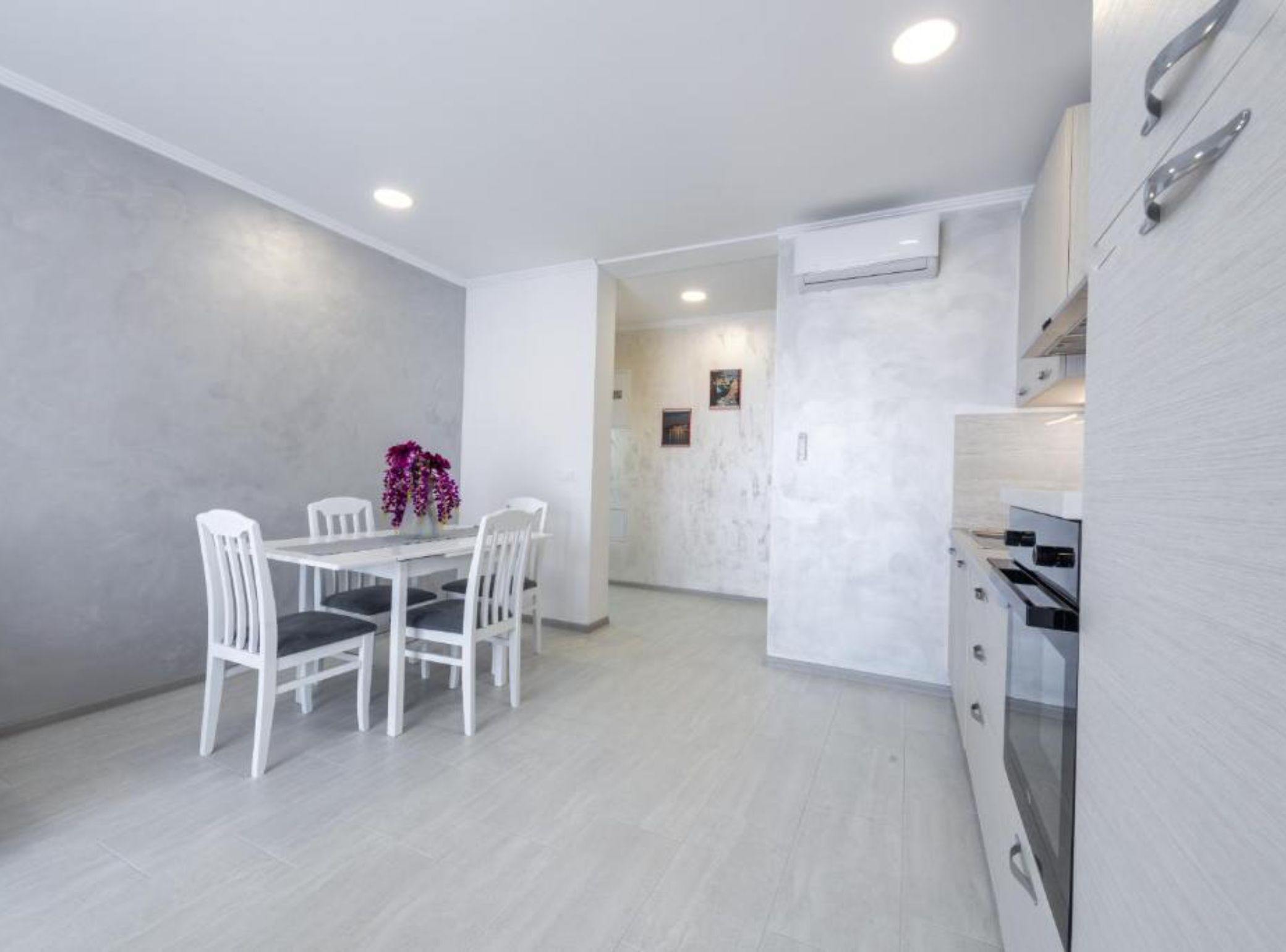 A modern kitchen with white cabinets, a dining table with chairs, and a small decorative plant.