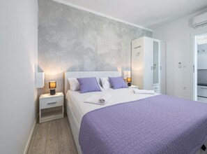 A bedroom with a bed, nightstands, a wardrobe, and a wall-mounted air conditioning unit. - Lumina Sea Apartments Cavtat (Konavle)