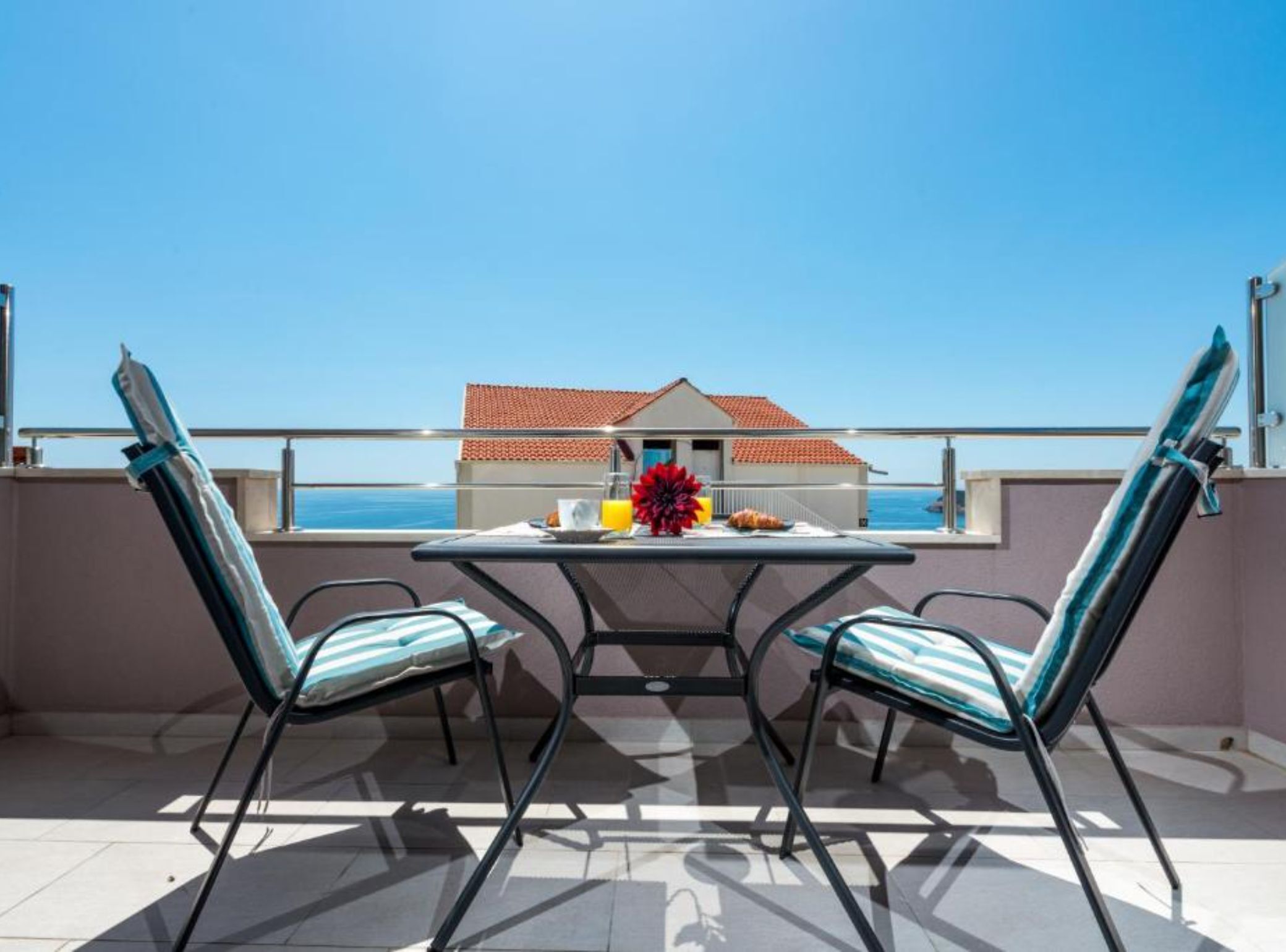 Un balcon avec deux chaises, une table et une vue sur un immeuble dont le toit est rouge.
