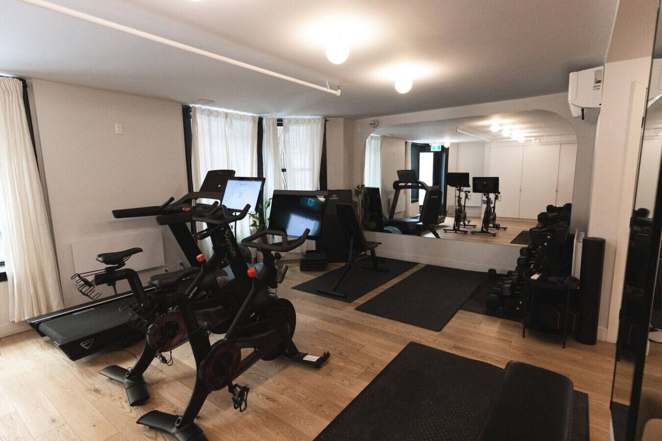 Een sportzaal thuis met fitnessapparatuur, een loopband, hometrainers en een spiegel die de ruimte weerspiegelt.