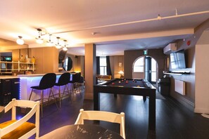 Eine Bar mit Hockstühlen, einem Billardtisch und einem Fernseher.