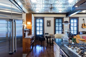 Eine moderne Küche mit Edelstahlkühlschrank, Holzschränken, einem Essbereich mit Tisch und Stühlen sowie einer Kücheninsel mit Spüle und Arbeitsplatte.