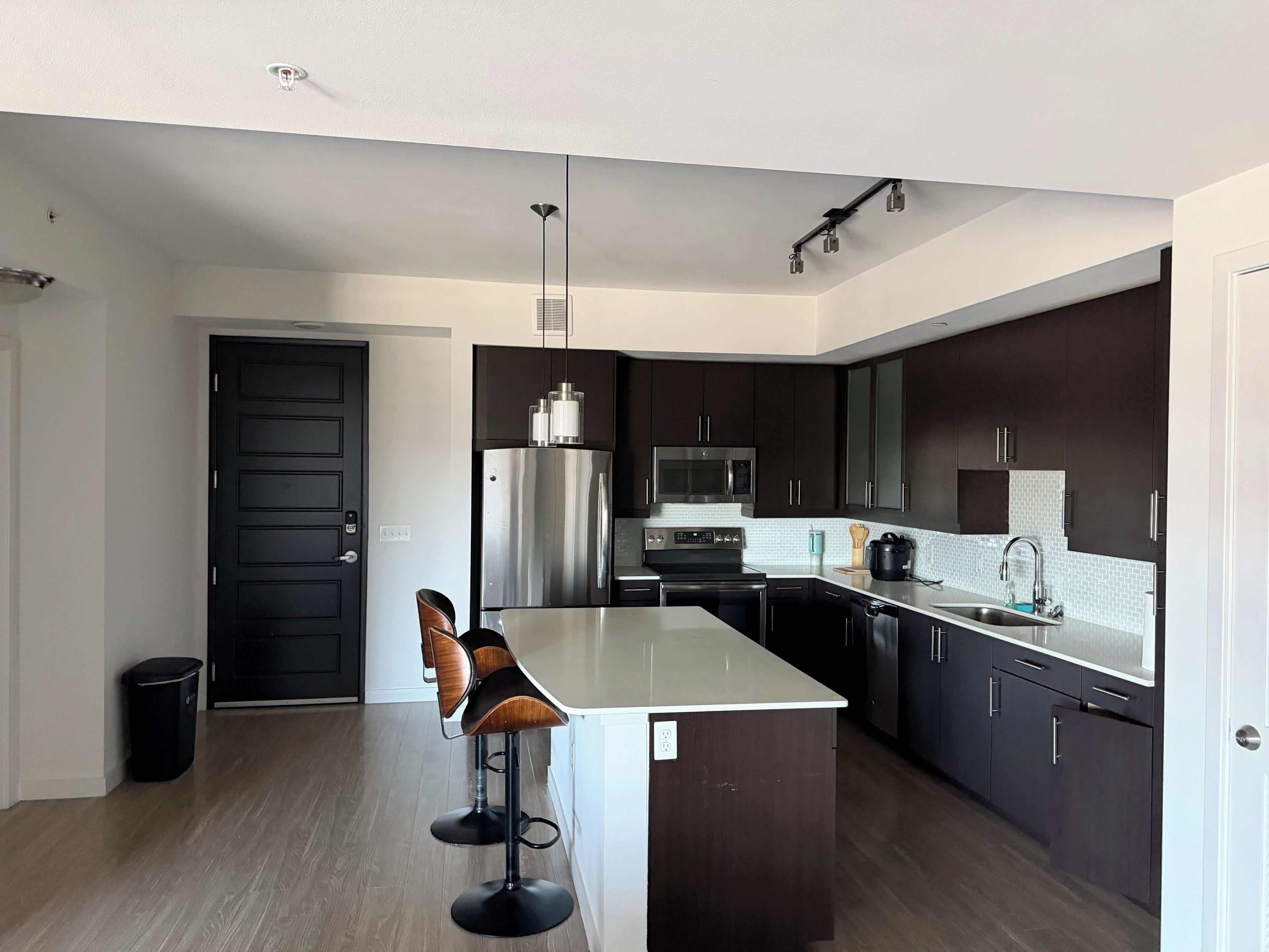 Une cuisine moderne avec des meubles de couleur sombre, des appareils en acier inoxydable, un îlot central et des tabourets de bar.