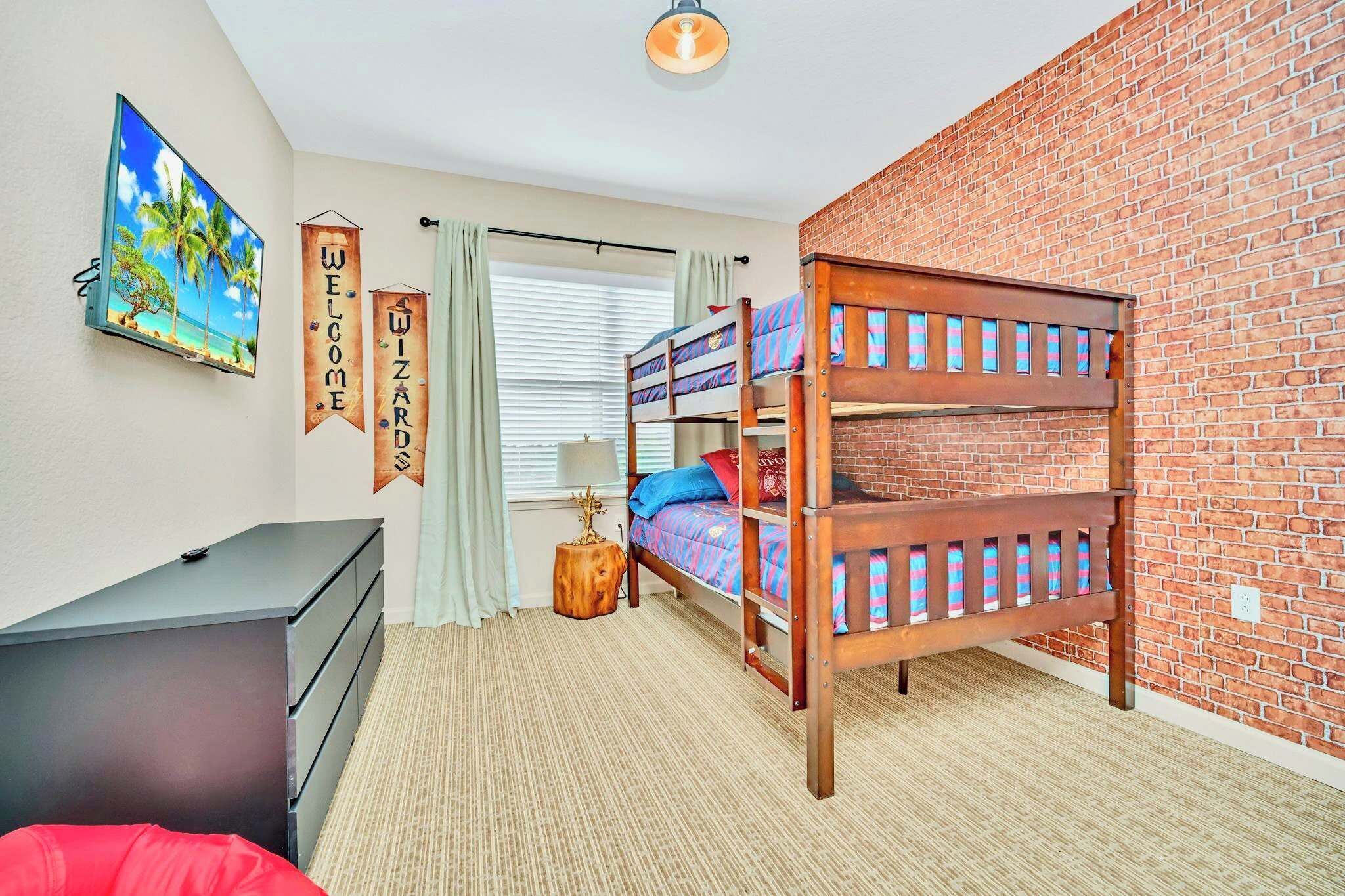 A room with bunk beds, a TV, a dresser, and a brick wall.