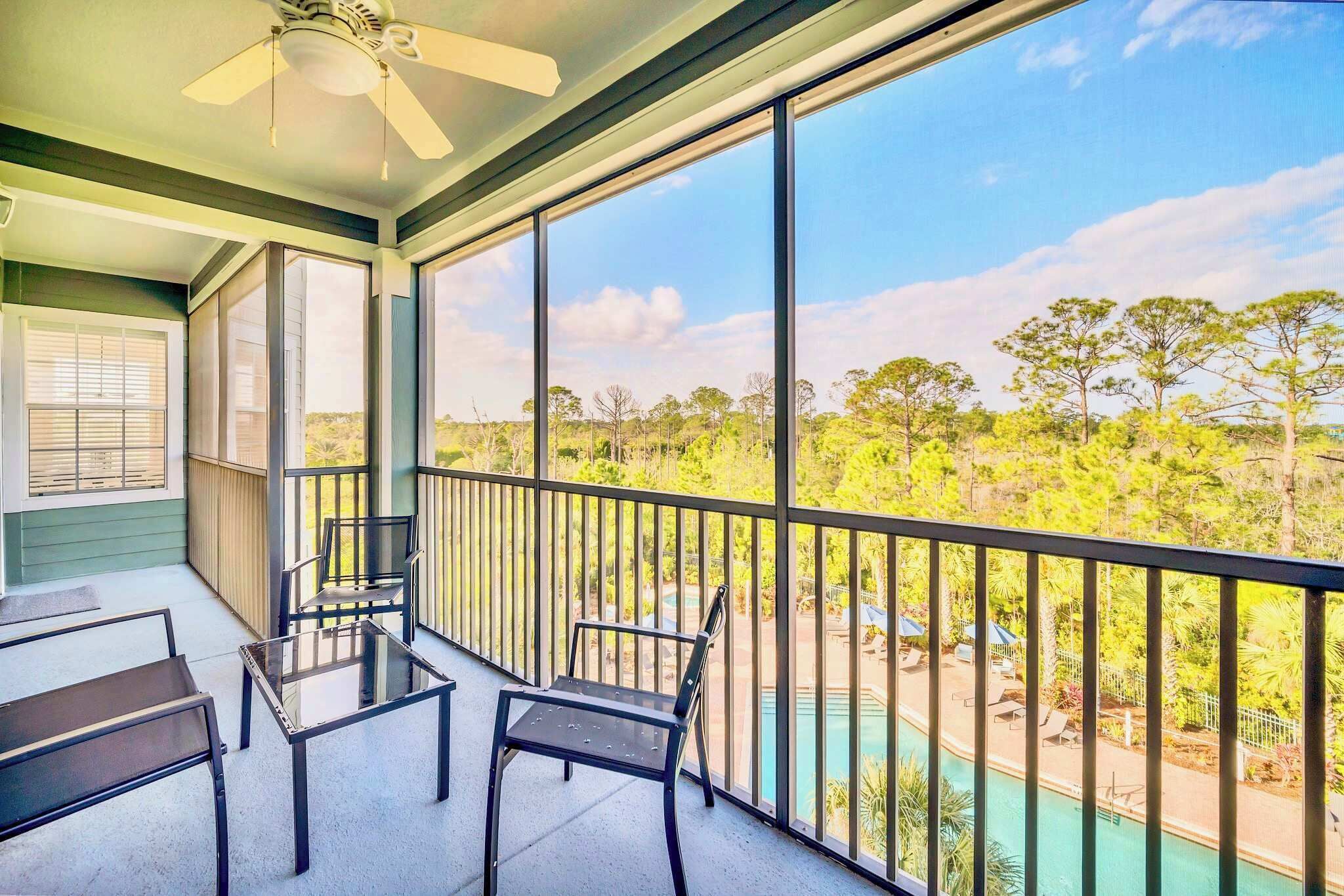 A balcony with a glass table and chairs, overlooking a pool and lush greenery.