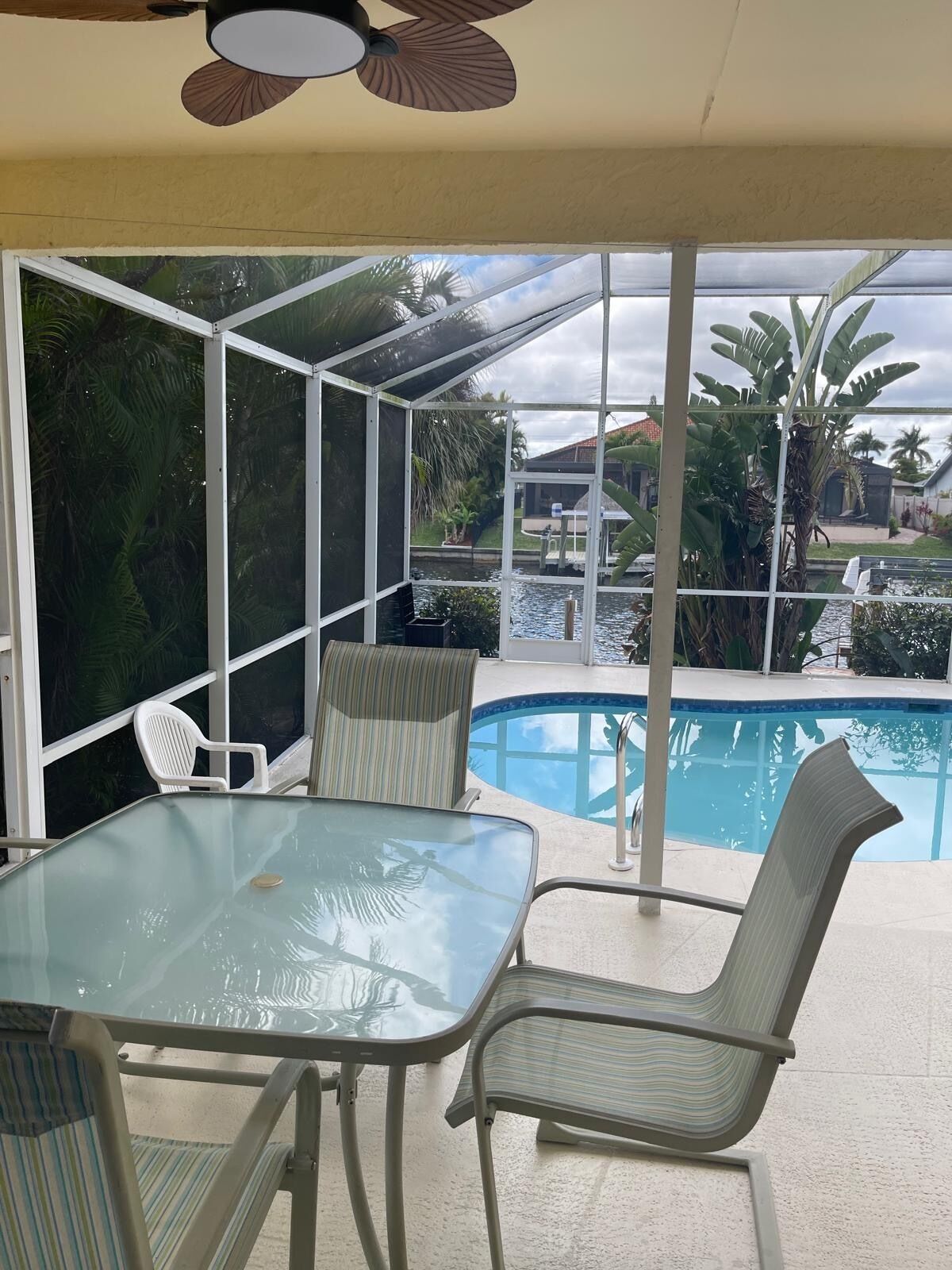 A glass-enclosed patio with a pool, a table, and chairs.