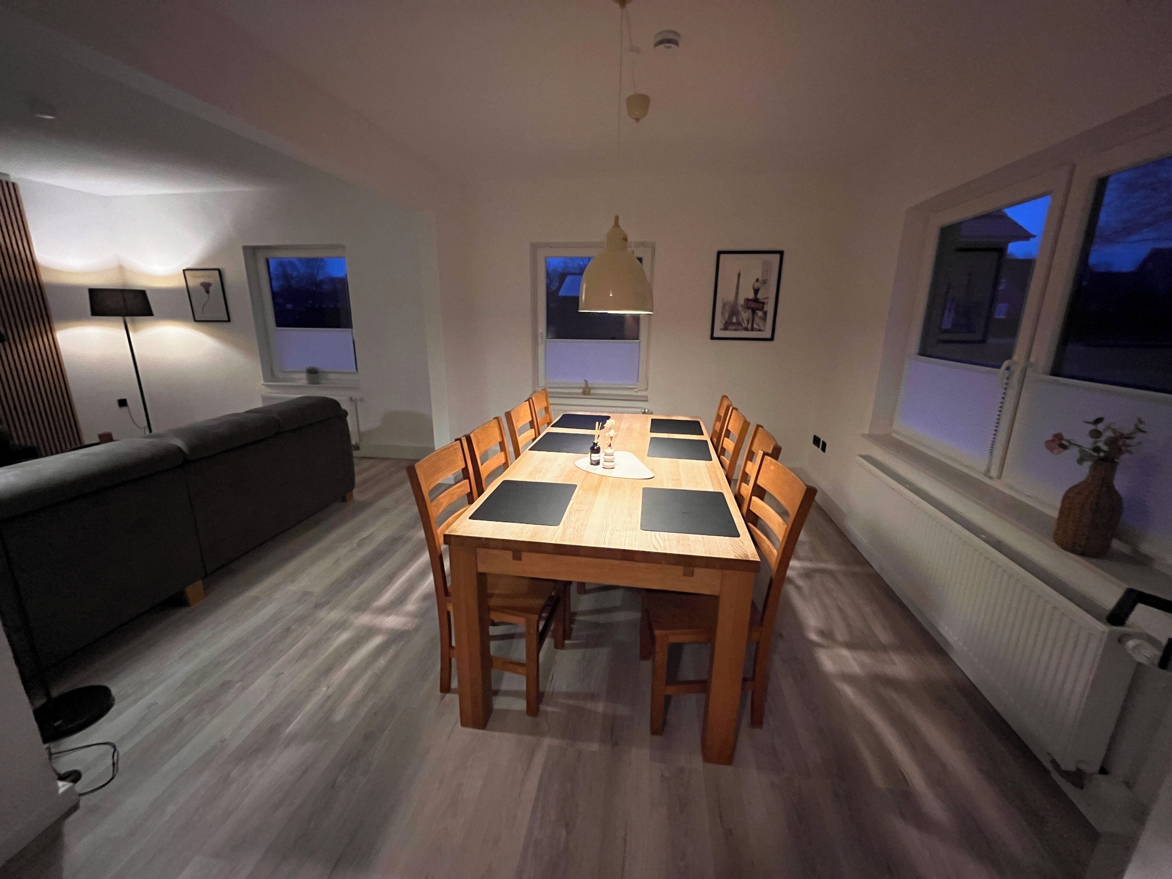 A dining area with a wooden table and chairs, a sofa, and a window with a view.