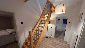 Eine Holztreppe mit einer Pendelleuchte, einem Bett, einem Heizkörper und einer weißen Wand.