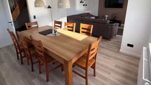 Ein stilvoller Wohnbereich mit Essplatz, ausgestattet mit einem Holztisch und Stühlen, einer Couch, einem Fernseher und Pendelleuchten.
