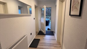 Ein Flur mit Heizkörper, einer zur Außenseite führenden Tür und einem gerahmten Bild an der Wand.