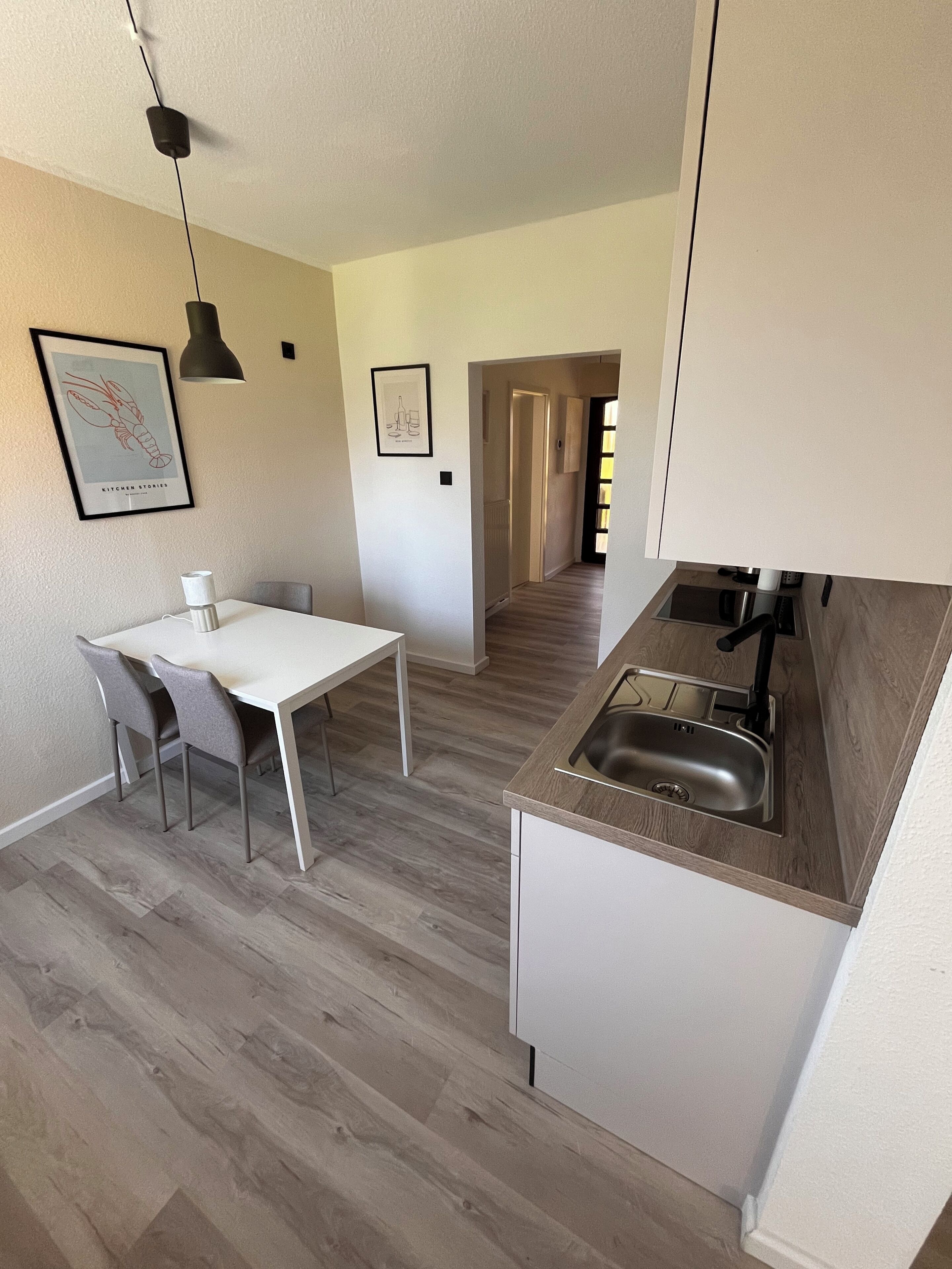 A modern kitchen with a white countertop, stainless steel sink, and a dining area with a white table and chairs.