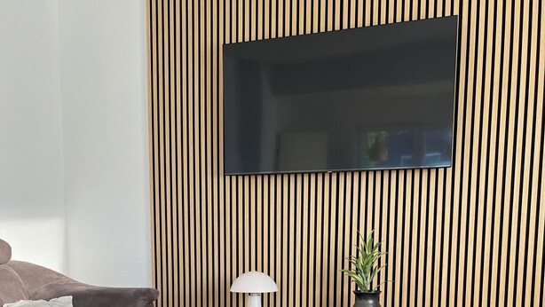 Ein modernes Wohnzimmer mit einer Couch, zwei runden Tischen, einer Lampe, einem Fernseher und einer Holzverkleidung.