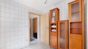 Una stanza con pavimento piastrellato, un armadio in legno con ante in vetro e una porta che dà su un'altra stanza.