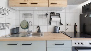 Una cucina con mobili in legno, un lavello in acciaio inox, un bollitore, un supporto per bollitore, un espositore per piatti e un frigorifero.