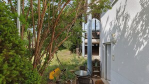 Un patio con tavolo e sedie, immerso nel verde e adiacente a un edificio bianco.