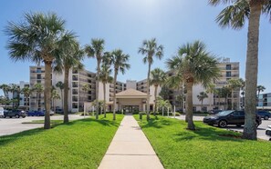 A hotel with a central entrance, surrounded by palm trees and a parking lot. - Anastasia #605 Ocean front property with panoramic view of ocean/beach, boat parking (St. Augustine Beach)