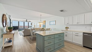 Une cuisine moderne dotée d’un îlot central, de meubles blancs et offrant une vue sur l’extérieur.