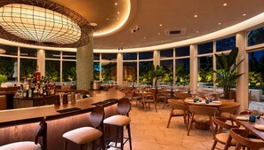 A spacious indoor area with a bar, multiple seating arrangements, and large windows providing views of the outdoors. - Ellipse Resort, Grace Bay /Jr Suite One Bedroom with Grace Bay Street View (Grace Bay)
